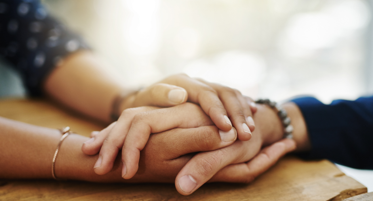Two people are supporting one another by holding hands. They have light and medium light skin.
