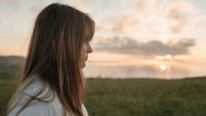 A woman is turned so you can see the side of her face. She is looking out in the distance, and seems empty.