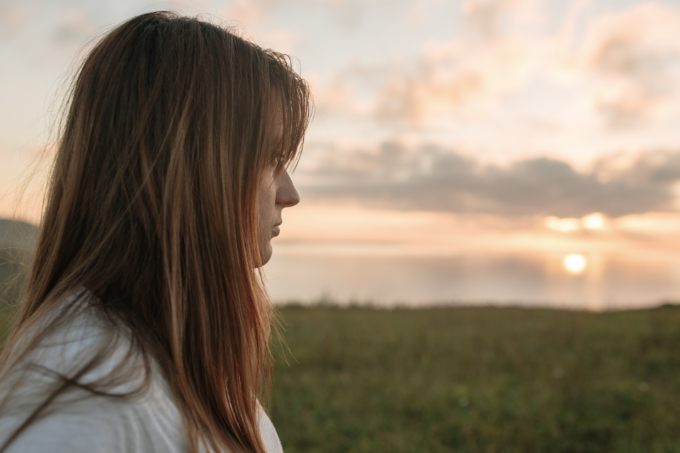 A woman is turned so you can see the side of her face. She is looking out in the distance, and seems empty.