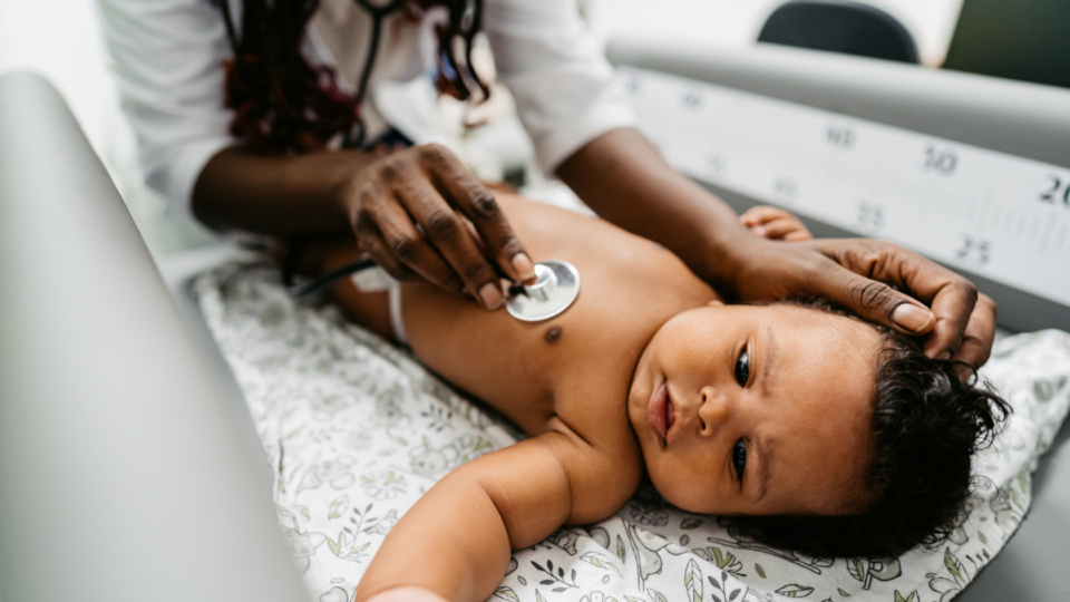 Baby lying on back as a doctor listens to their heart using a stethoscope.