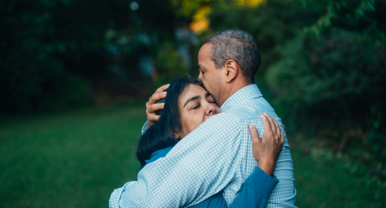 A man and a woman standing outside, hugging.