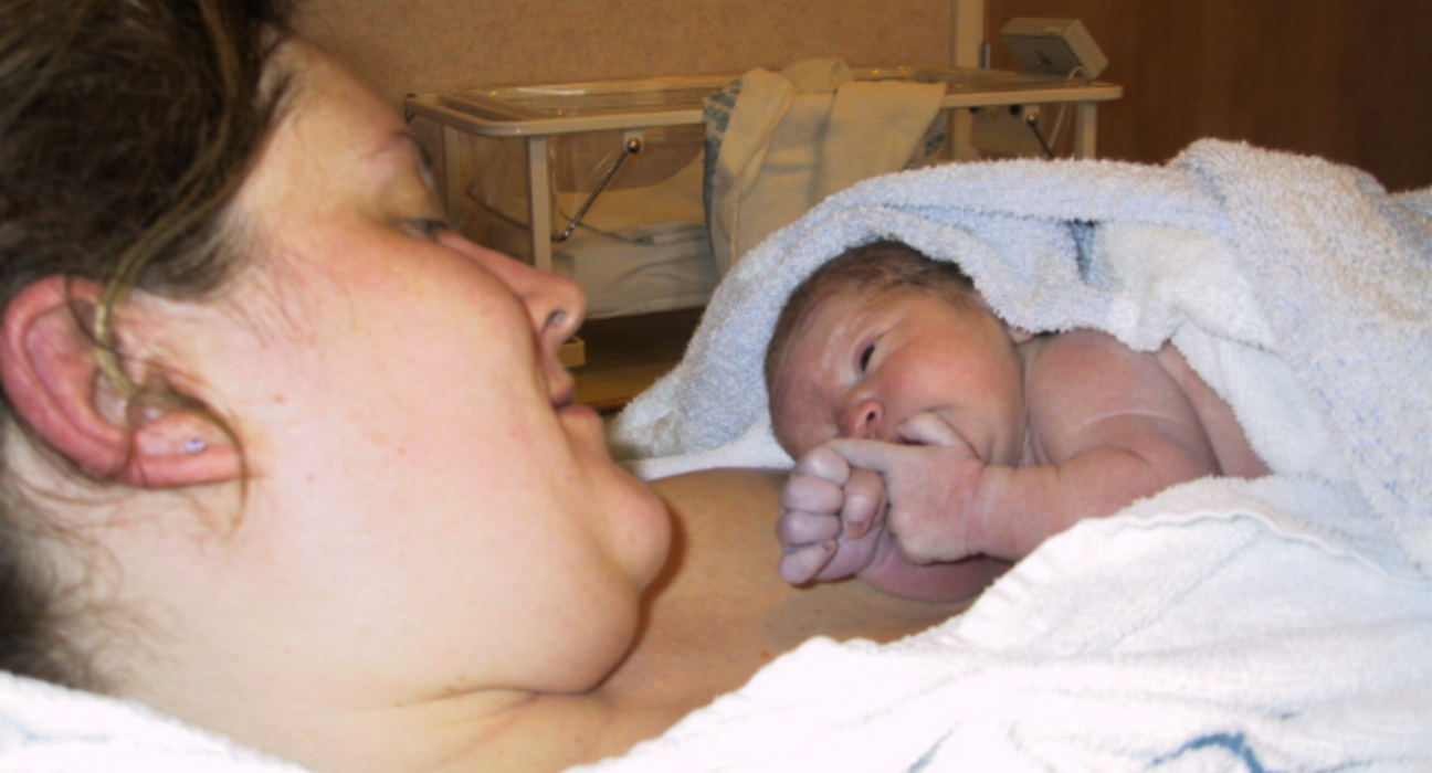 Louise is holding Ellis after giving birth. He is in her arms in hospital and she is looking down at him.