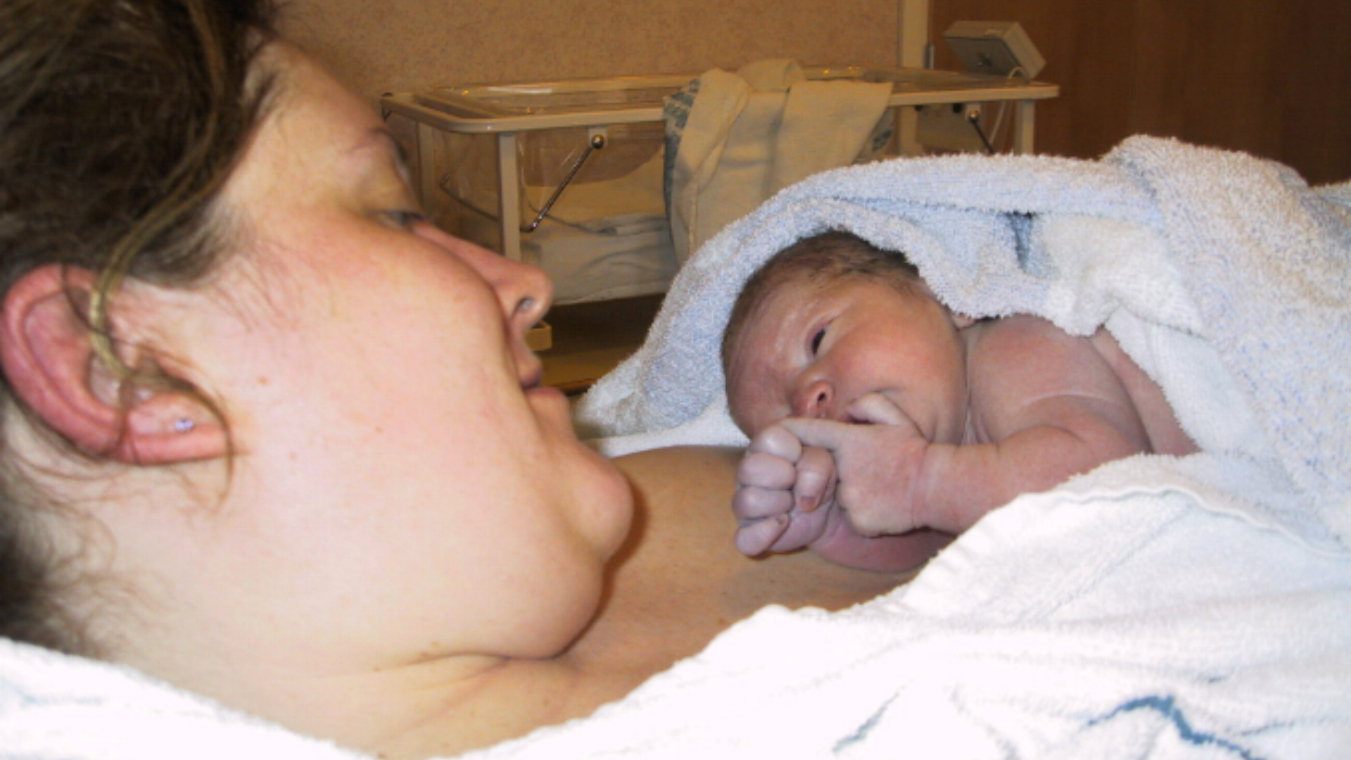 Louise is holding Ellis after giving birth. He is in her arms in hospital and she is looking down at him.