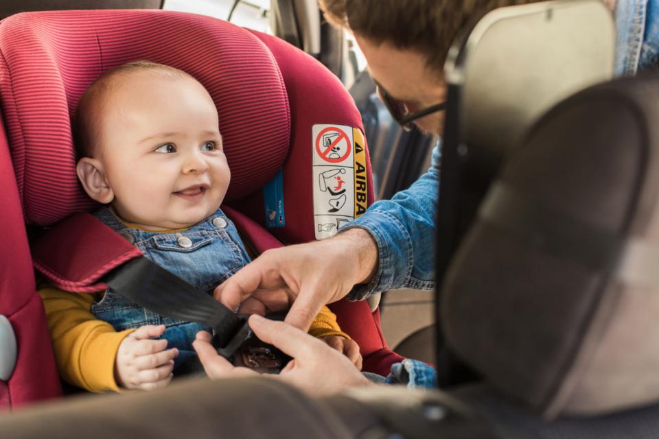 Smiling baby being fastened into a carseat.