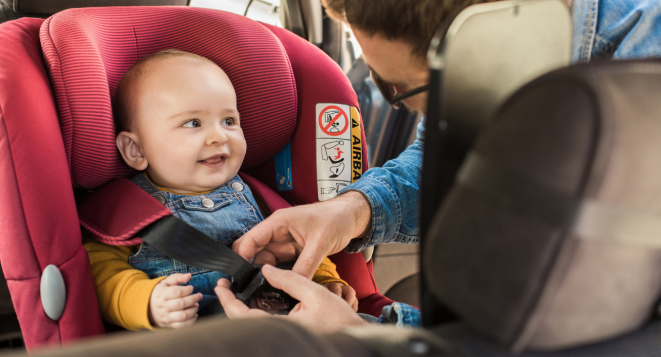 Smiling baby being fastened into a carseat.