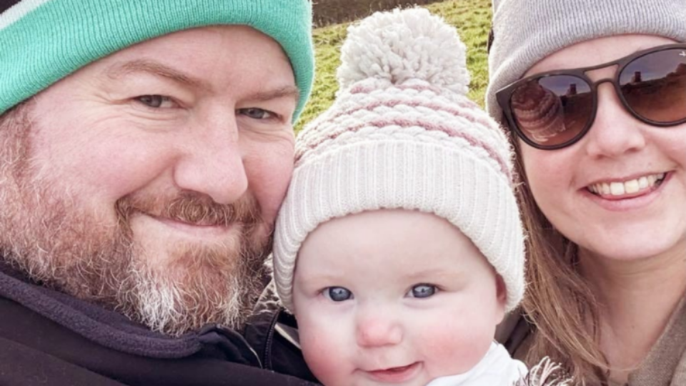 James and Camila outfoors, holding their baby Sophia, all wearing wooly hats.