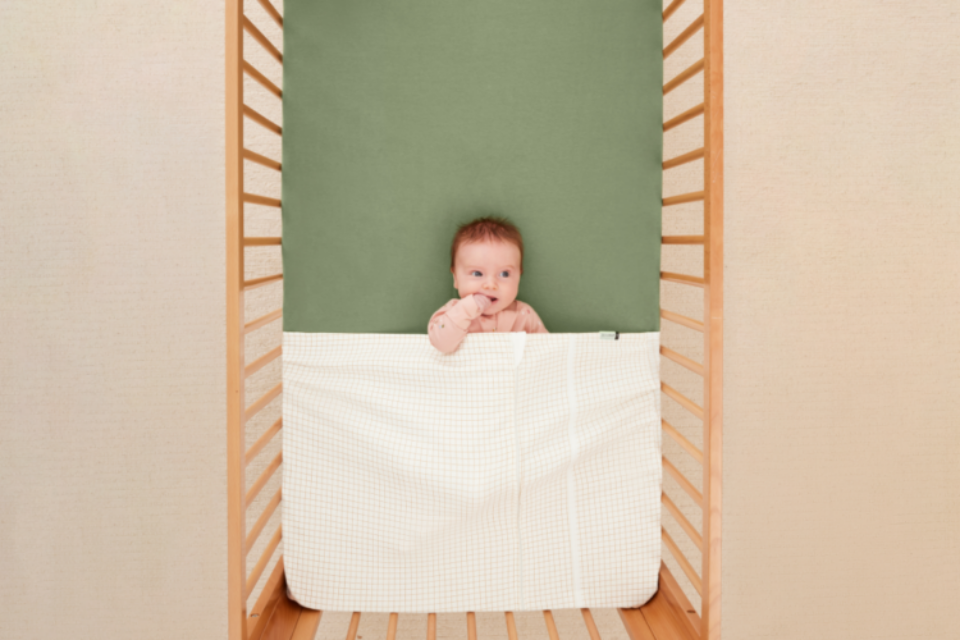 An image of a baby in a cot with a cot safely tucked beneath their armpits.
