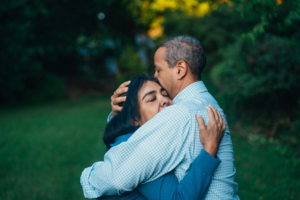 A man and a woman standing outside, hugging.