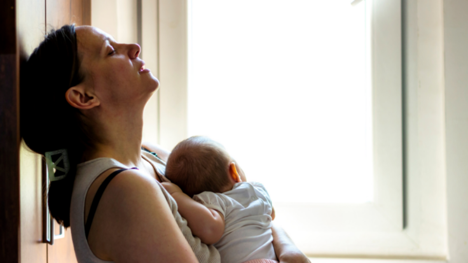 Lady holding her baby, leaning her head back on the wall.