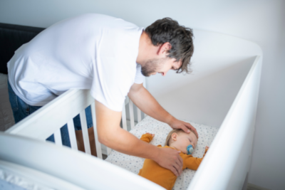 Dad checking on baby sleeping in their cot with a dummy in.