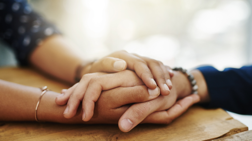Two people are supporting one another by holding hands. They have light and medium light skin.