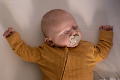 A baby is asleep in a safer sleep position, on their back with a clear cot. They have a dummy in their mouth