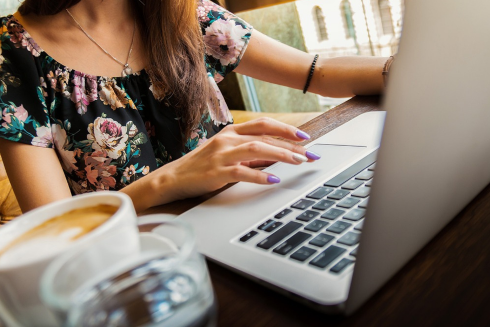Lady sitting at desk on her laptop, with a coffee.