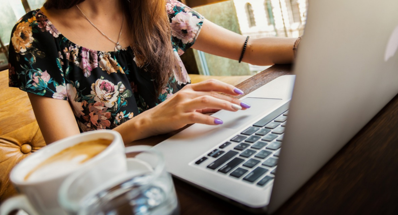 Lady sitting at desk on her laptop, with a coffee.