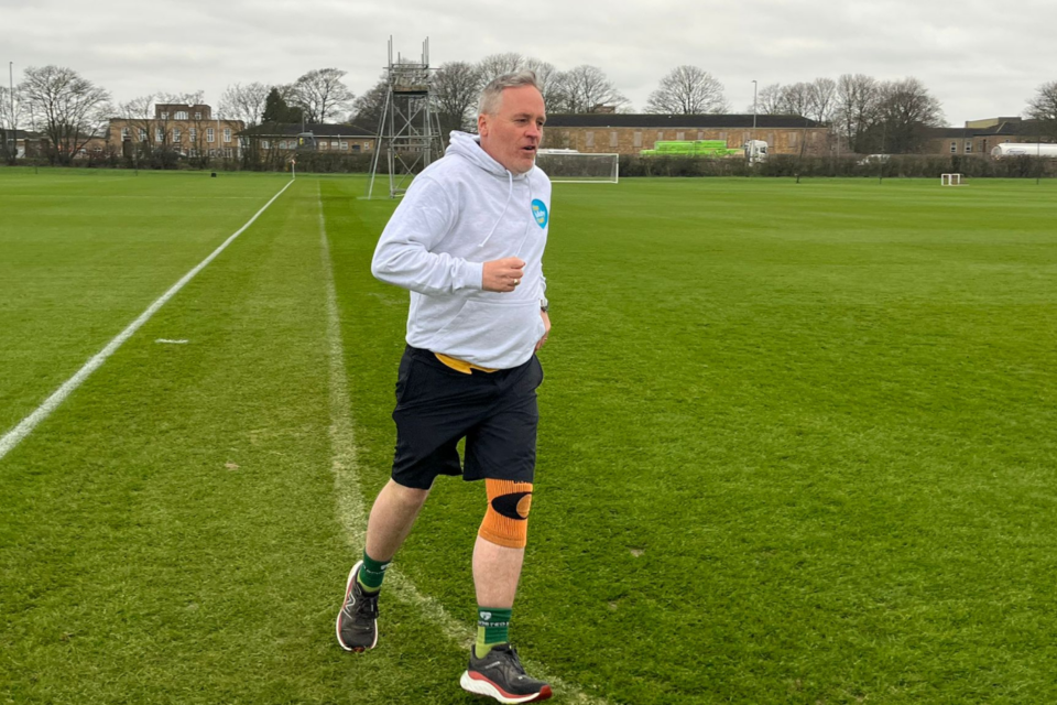 Karl wearing a grey jumper, running around a large green open space.