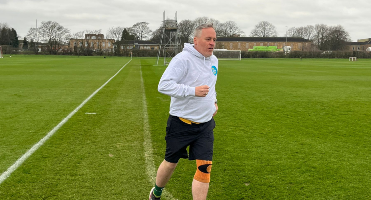 Karl wearing a grey jumper, running around a large green open space.