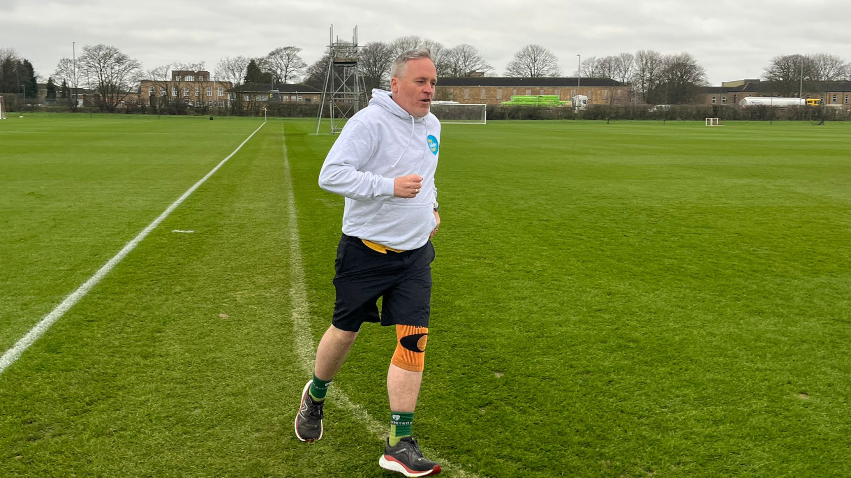 Karl wearing a grey jumper, running around a large green open space.