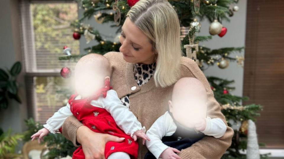 Jess holding her twins and standing in front of a Christmas tree.