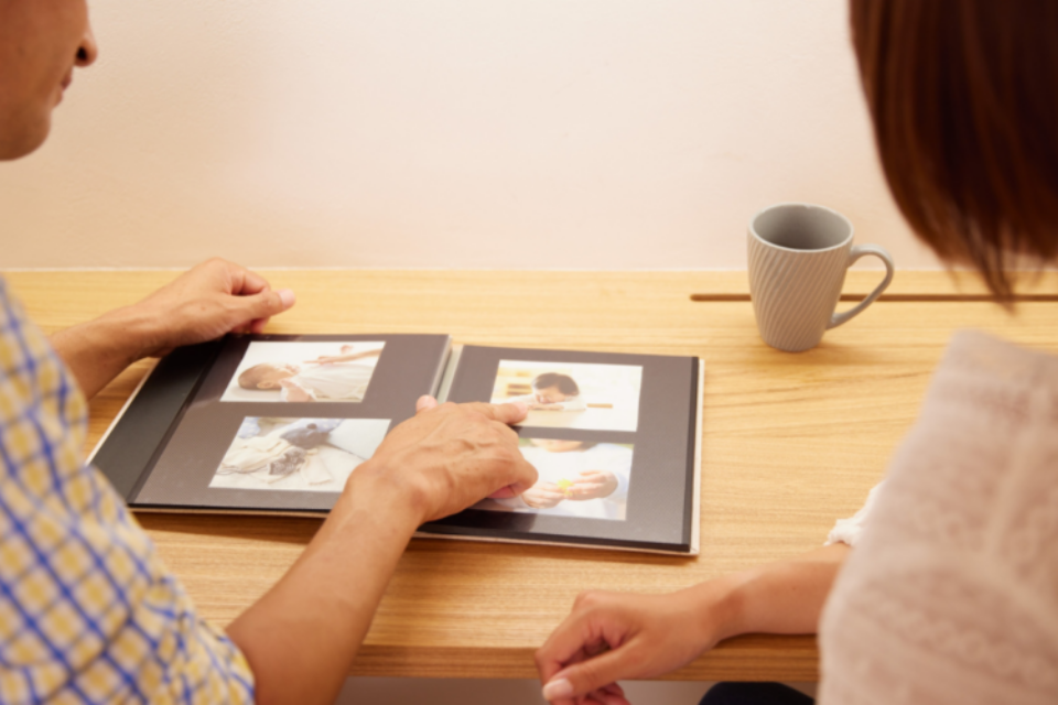 Couple with their backs to the camera, looking at a memory book together of their baby. Pointing at the images.