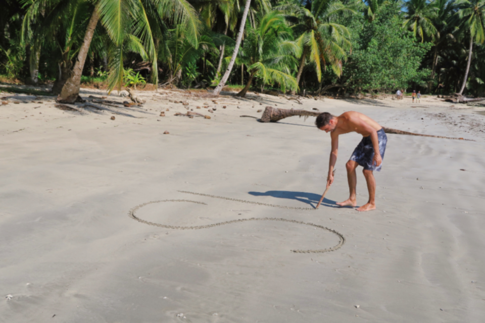 Man using a stick to write in the sand.