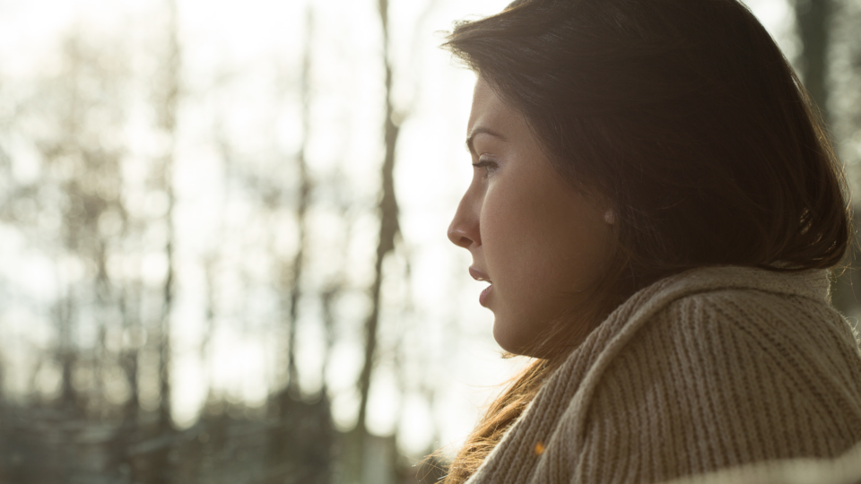 A young woman is looking out of the window, and from her side profile you can tell that she is visibly distressed or upset.