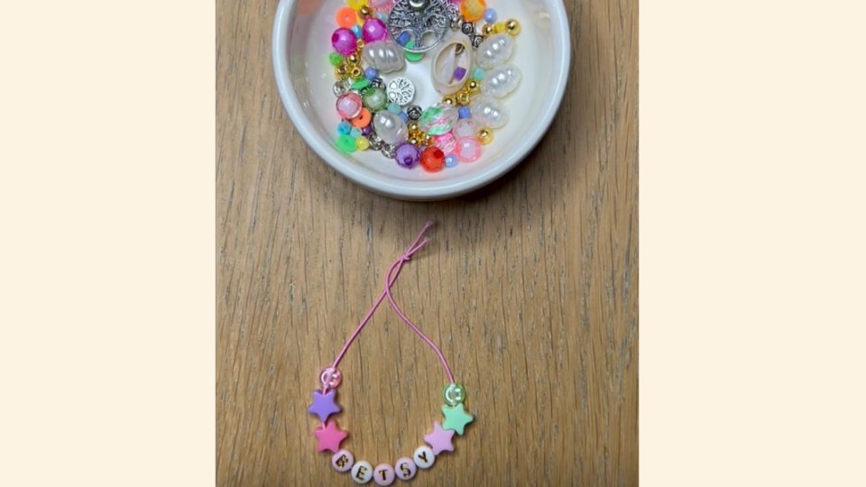 Bracelet that says a child name, that has just been crafted. There is a bowl of beads above it.