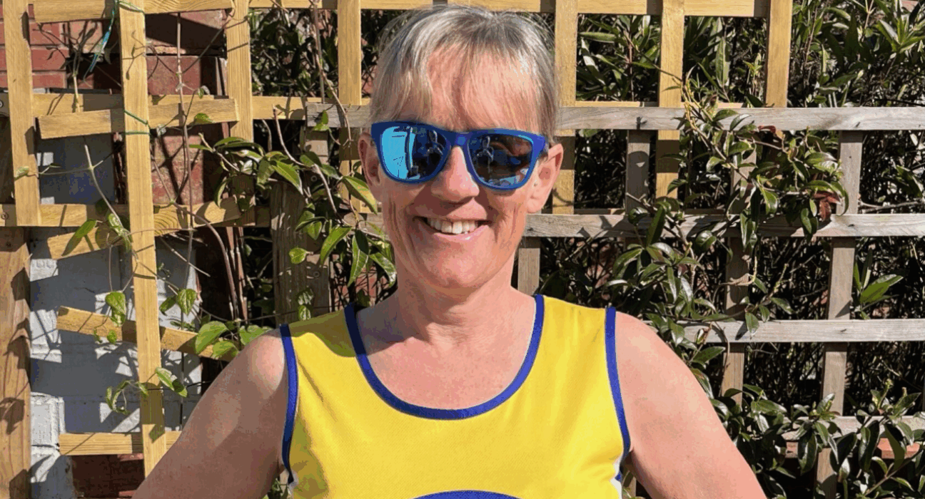 Clare wearing sunglasses and her Lullaby Trust vest, standing outdoors smiling at the camera.