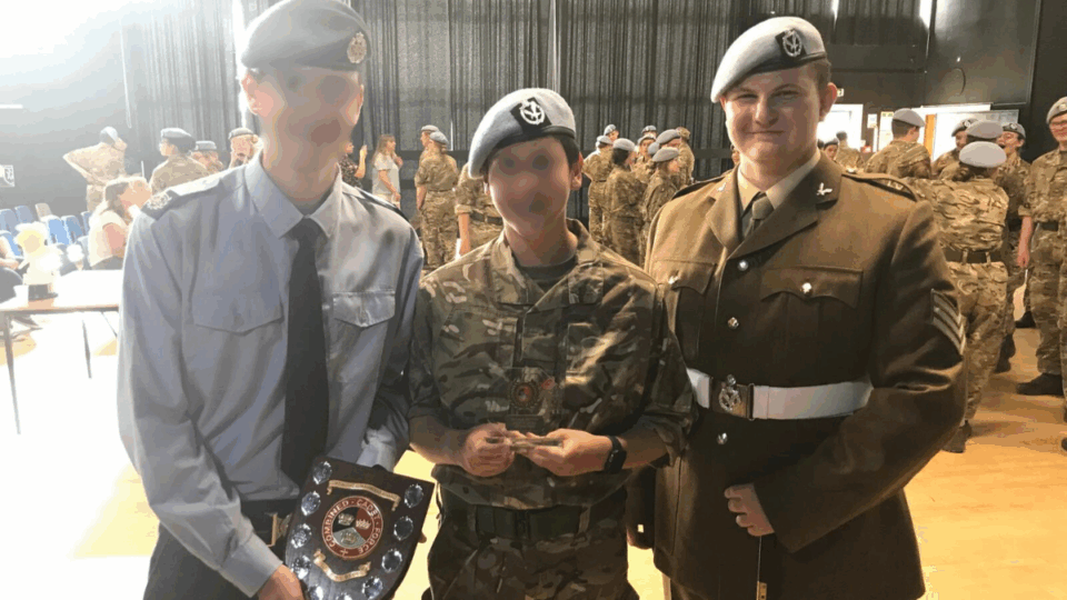 Matt wearing his army uniform, standing next to two others. He is standing up straight with his arms behind his back, smiling at the camera.