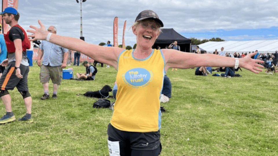 Clare wearing a Lullaby Trust t-shirt, ready for a run with her arms spread wide and smiling.
