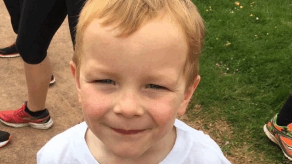 Clare's little boy smiling up at the camera, wearing a white t-shirt.