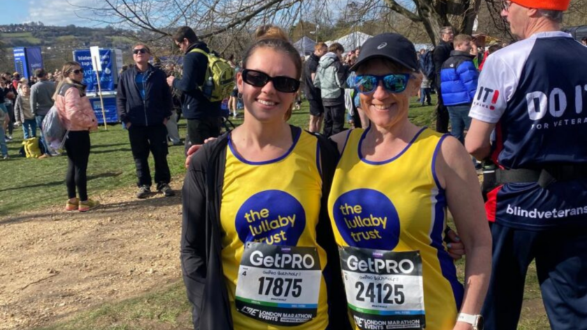 Georgie and Clare wearing their Lullaby Trust running vests at the London Marathon, with their arms around each other.