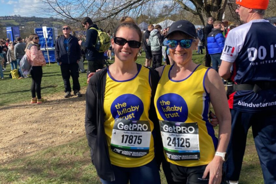 Georgie and Clare wearing their Lullaby Trust running vests at the London Marathon, with their arms around each other.