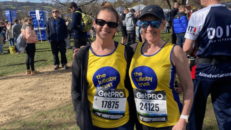 Georgie and Clare wearing their Lullaby Trust running vests at the London Marathon, with their arms around each other.
