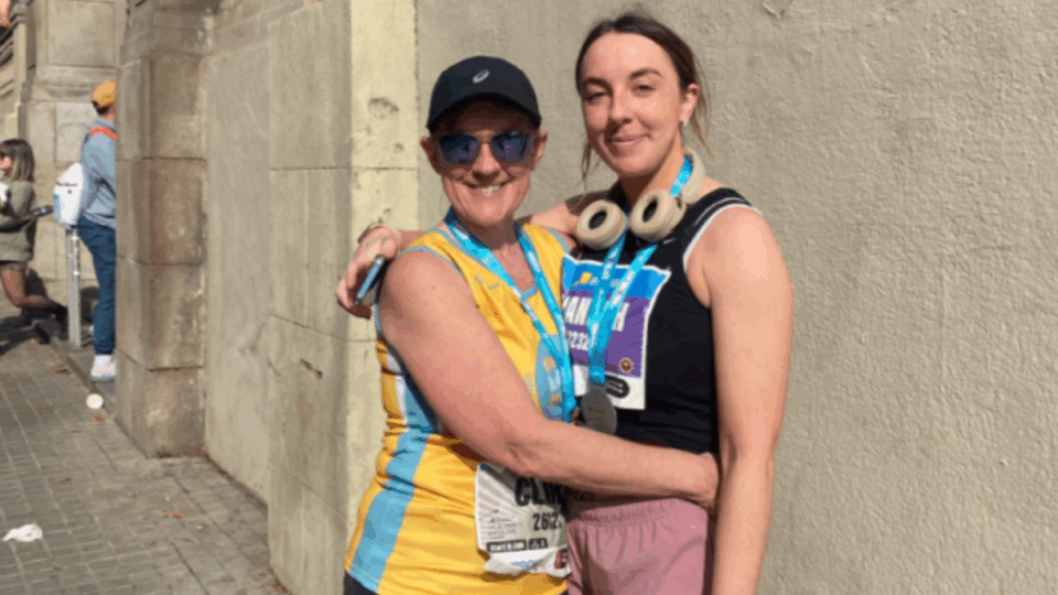 Clare and Georgie at a running event, arms around each other smiling at the camera, wearing their medals.