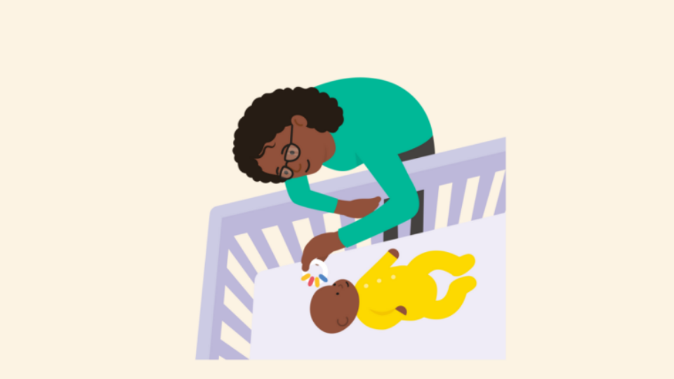 Mother wearing a green top, playing with her baby who is in its cot.