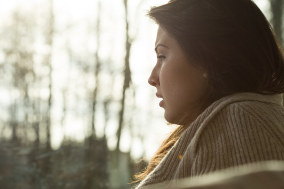 A young woman is looking out of the window, and from her side profile you can tell that she is visibly distressed or upset.