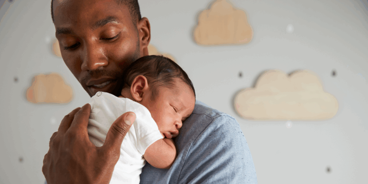 A dad is holding a very young baby on his shoulder. His hand is caressing the baby's back, and he's looking down at the baby.