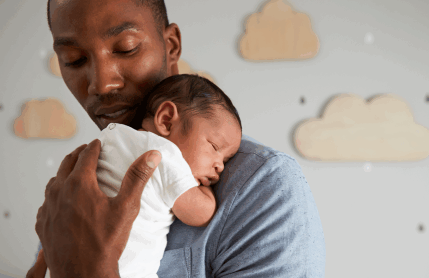 A dad is holding a very young baby on his shoulder. His hand is caressing the baby's back, and he's looking down at the baby.