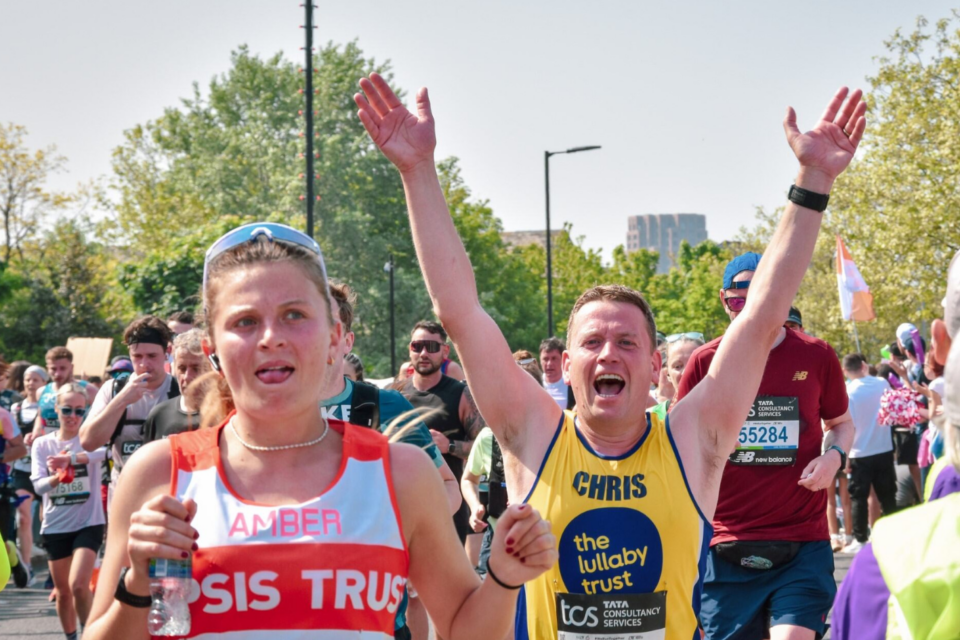 Marathon runner wearing Lullaby Trust vest cheering with his arms up in the air, running the race.