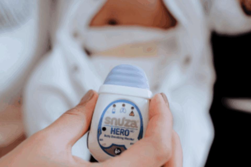 Snuza HeroMD monitor being held up with a baby in a babygrow in the background.