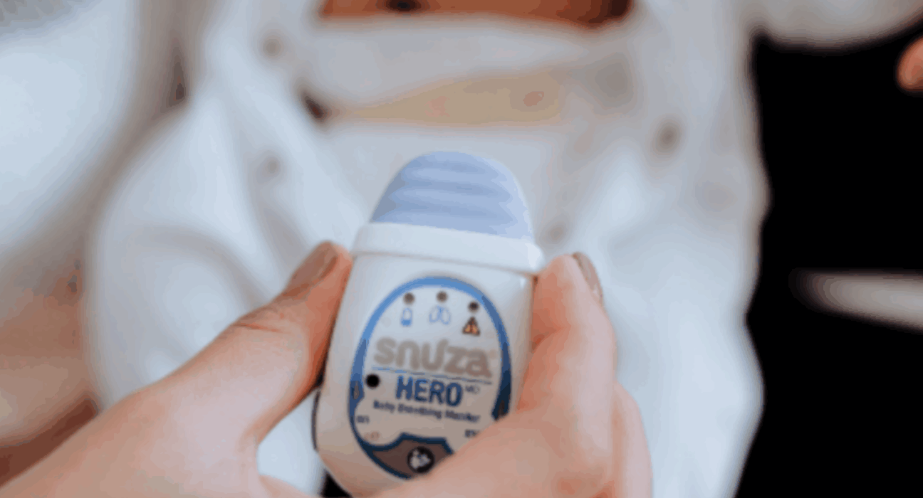 Snuza HeroMD monitor being held up with a baby in a babygrow in the background.