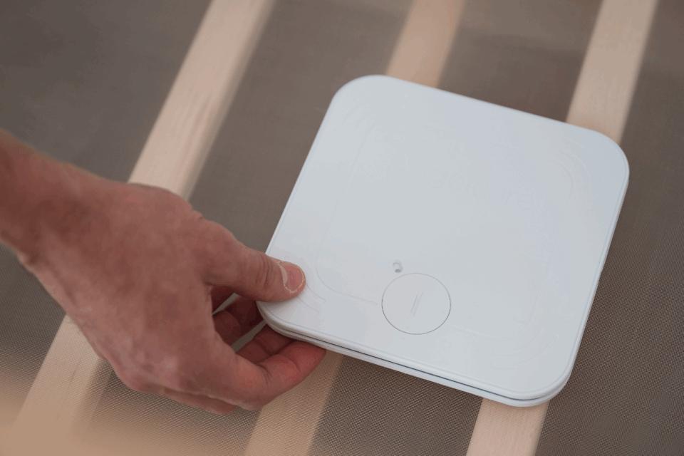 A hand is placing a monitor beneath a baby mattress in a cot