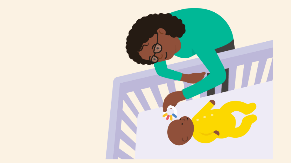 Mother wearing a green top, playing with her baby who is in its cot.