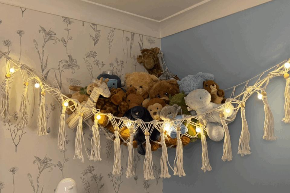 A pile of toys sitting on a fabric shelf, high up in the corner of a bedroom.