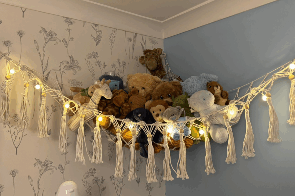 A pile of toys sitting on a fabric shelf, high up in the corner of a bedroom.