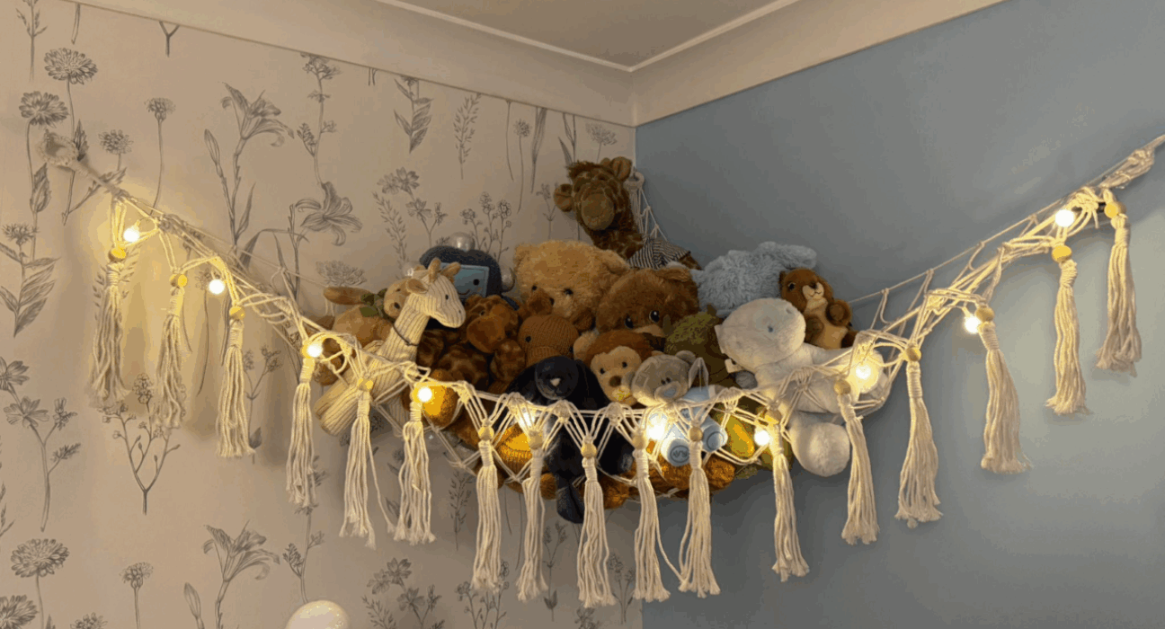 A pile of toys sitting on a fabric shelf, high up in the corner of a bedroom.