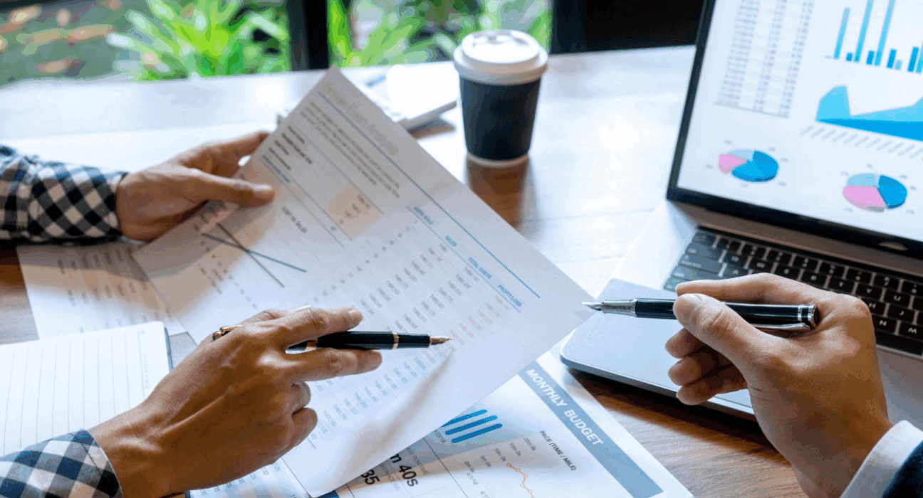 People's hands holding pens, inspecting graphs and data on sheets of paper.