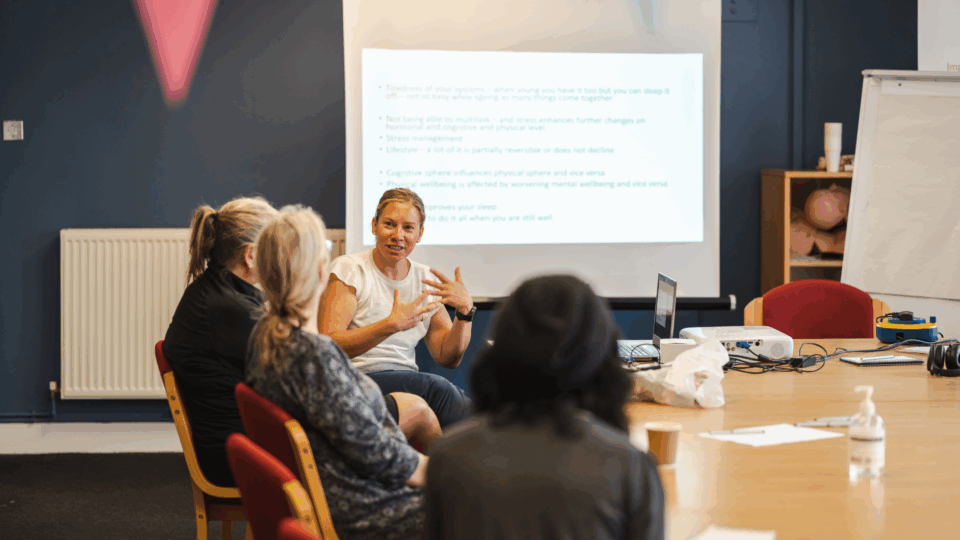 People sitting at a table having a meeting, with a presentation up on the board.