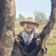 Carol wearing a hat, standing between the branches of a tree.