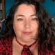Clare with dark curly hair, wearing a red and black top.